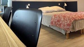 A modern bedroom with a bed, two chairs, a desk, and a nightstand.