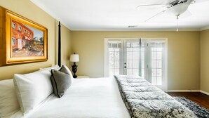 A hotel room with a large bed, a painting on the wall, a lamp, and a view of the outside through a window.