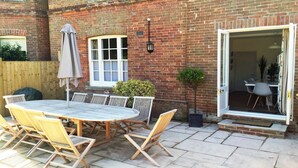 A brick building with a patio area featuring a round table and chairs, a potted plant, and a sliding glass door leading to an interior space. - Quay Corner Christchurch Dorset (Christchurch)