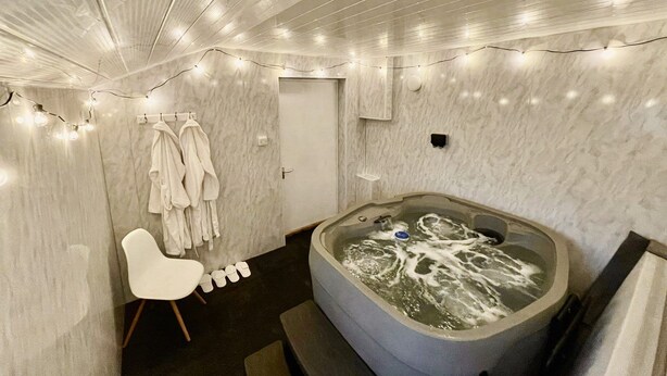 A modern bathroom with a large bathtub, marble walls, and string lights. - Quay Corner Christchurch Dorset (Christchurch)