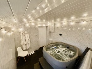 A modern bathroom with a large bathtub, marble walls, and string lights.