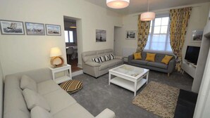 A living room with a sofa, a coffee table, a TV, and a lamp. - Quay Corner Christchurch Dorset (Christchurch)