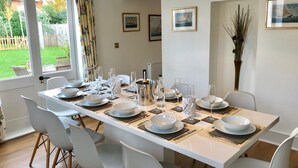 A dining area with a table set for six, white chairs, and a view of the garden through a door. - Quay Corner Christchurch Dorset (Christchurch)