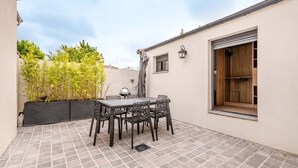 Eine Terrasse mit Tisch und Stühlen, ein Fenster mit Holztür und eine Wandleuchte.