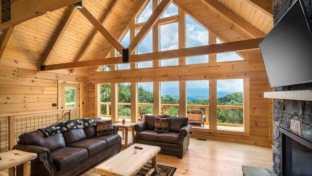 A spacious wooden cabin with a high ceiling, large windows, a fireplace, and a cozy seating area. - Four Bears: Amazing View, Private, Arcade, Screened in Porch with Wood Burning (Gatlinburg)