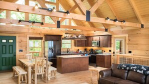 A spacious kitchen with wooden cabinetry, a central island, and a dining area with wooden furniture. - Four Bears: Amazing View, Private, Arcade, Screened in Porch with Wood Burning (Gatlinburg)