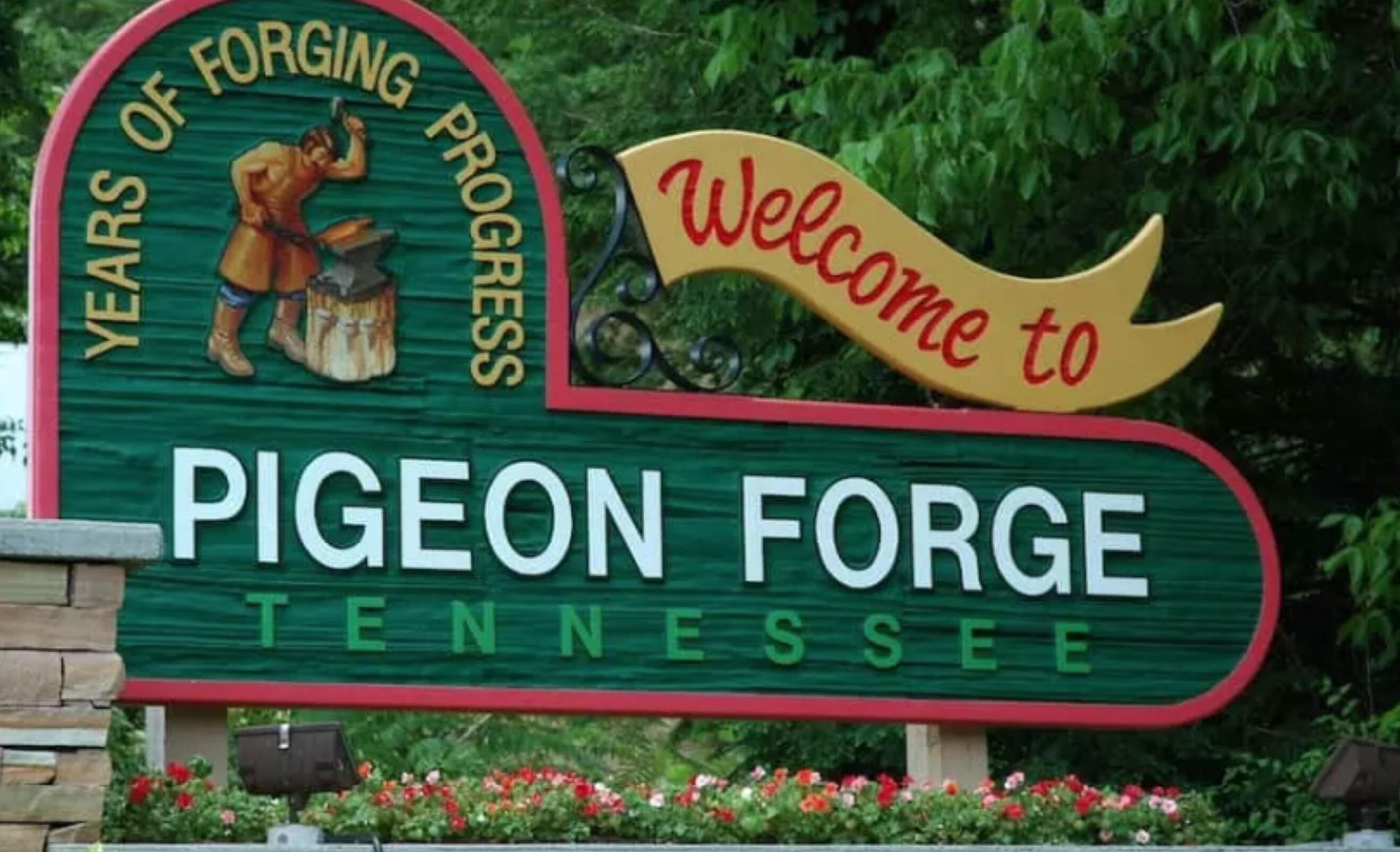 Un panneau d’accueil à l’entrée de Pigeon Forge, dans le Tennessee, avec un panneau noir et vert bordé de rouge, une boîte aux lettres noire et des fleurs rouges.