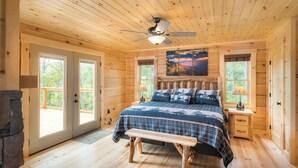 A wooden cabin bedroom with a bed, bench, ceiling fan, and large windows. - Four Bears: Amazing View, Private, Arcade, Screened in Porch with Wood Burning (Gatlinburg)