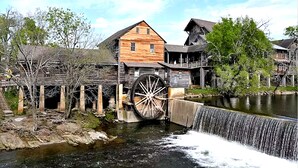 A historic wooden building with a large water wheel and a wooden bridge over a river. - Four Bears: Amazing View, Private, Arcade, Screened in Porch with Wood Burning (Gatlinburg)