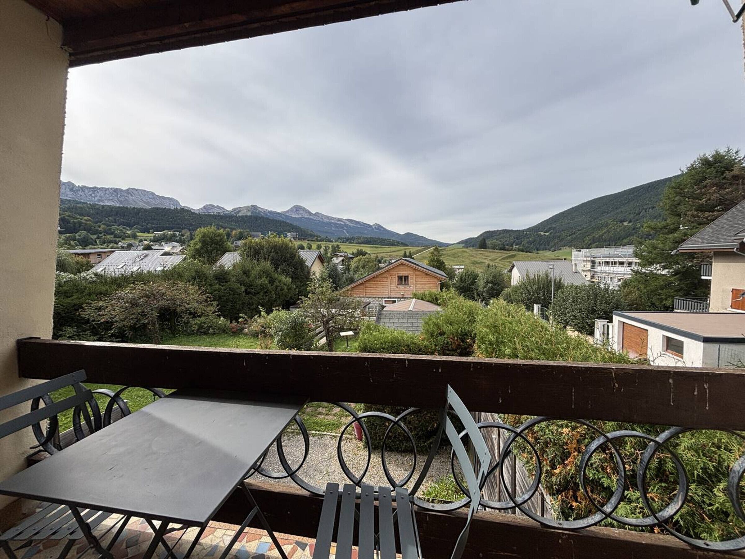 Un balcon offrant une vue sur un paysage montagneux, une cabane en bois et un bâtiment moderne.