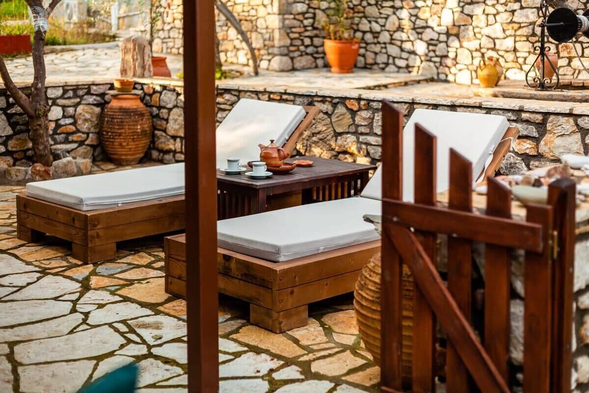 A stone-floored outdoor seating area with wooden loungers and a table with a teapot.