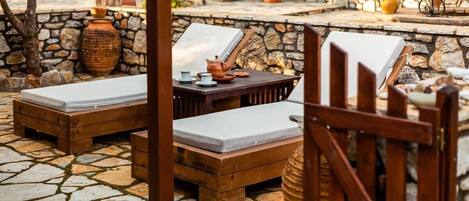 A stone-floored outdoor seating area with wooden loungers and a table with a teapot.
