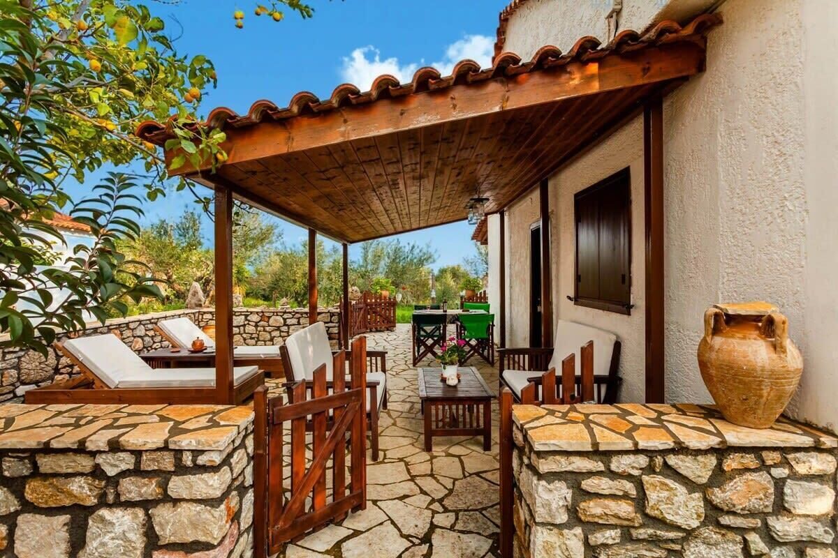 A covered outdoor patio with stone walls, wooden furniture, and a large vase.