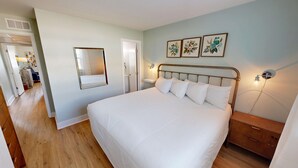 Ein Schlafzimmer mit einem großen Bett, einem Nachttisch, einem Spiegel und drei gerahmten Pflanzenbildern an der Wand.