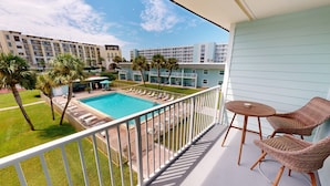 A balcony with a view of a swimming pool, lounge chairs, and a table. - Venus 308 overlooking pool Easy Beach Access by RedAwning (Fort Walton Beach)