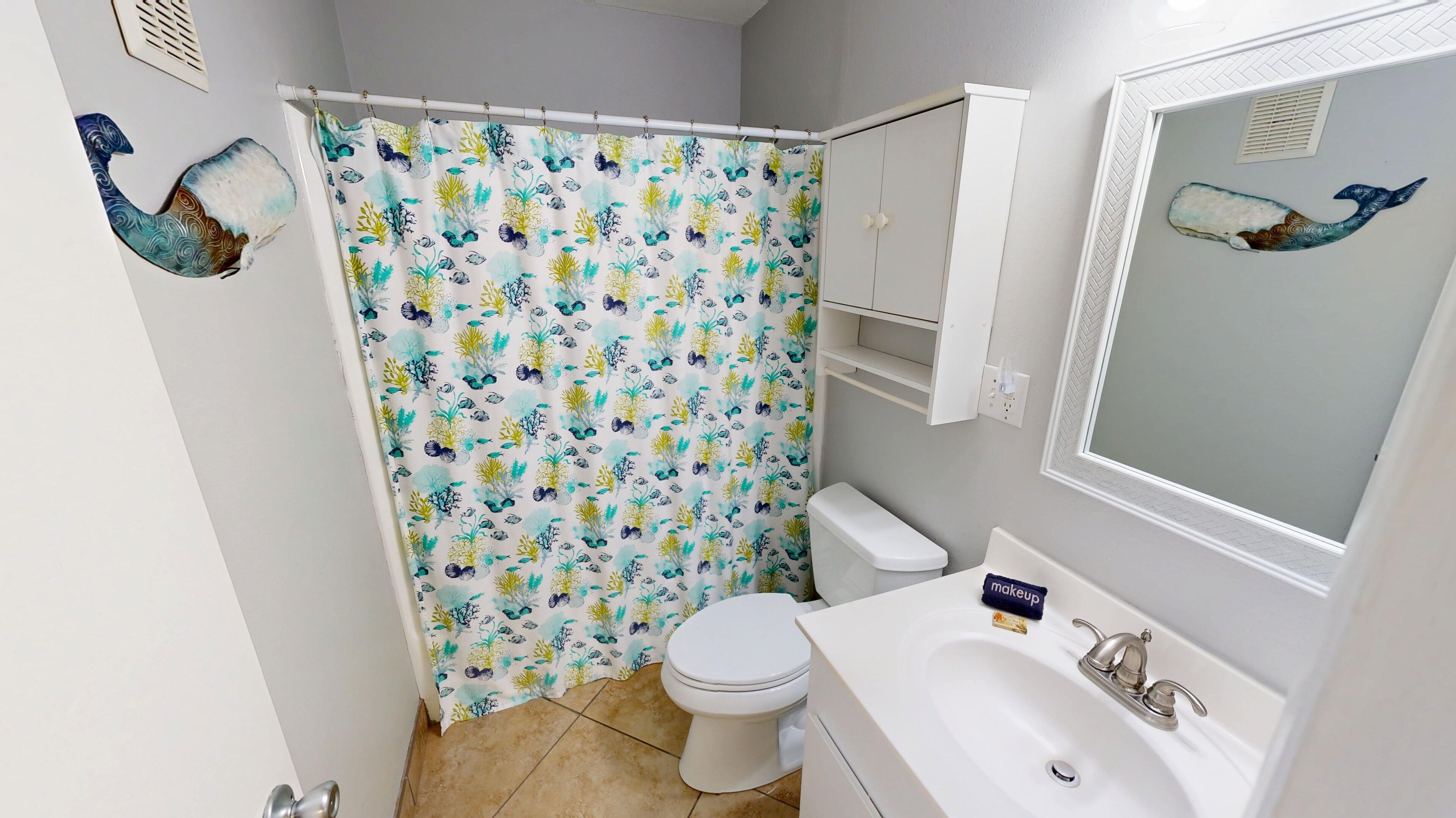 A bathroom with a shower curtain featuring a marine life pattern, a toilet, a sink with a mirror, and a towel rack.