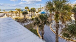 A beachside view with palm trees, a sandy path, and a building with a blue roof.