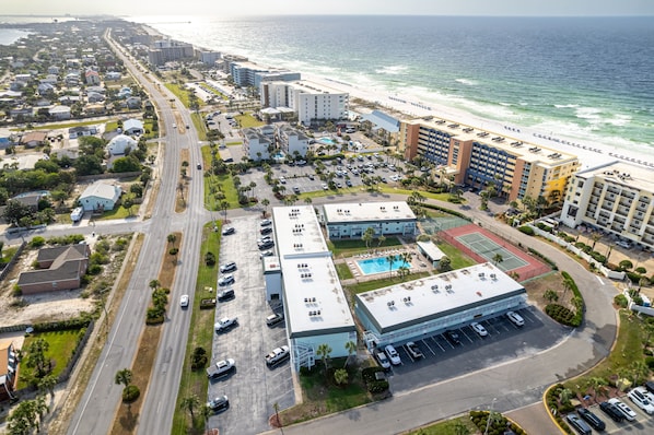 An aerial view of a coastal hotel with a swimming pool, parking lot, and beachfront access.