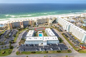 An aerial view of a hotel complex with multiple buildings, a swimming pool, and a beach in the background.