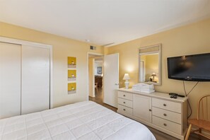 Una habitación de hotel con cama, televisor, cómoda y espejo.