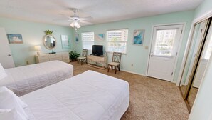 A bedroom with two beds, a TV, a desk, and a ceiling fan.