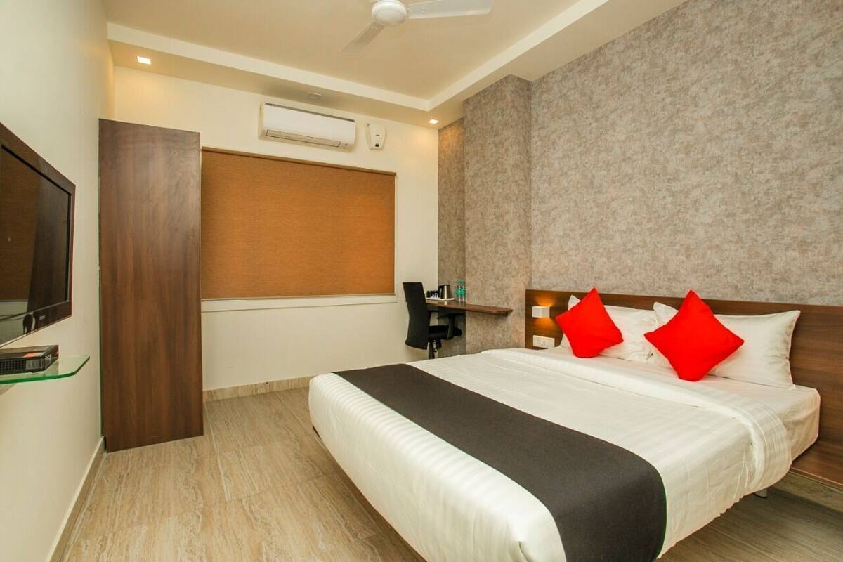 A hotel room with a bed, a desk, a chair, a TV, and an air conditioning unit.