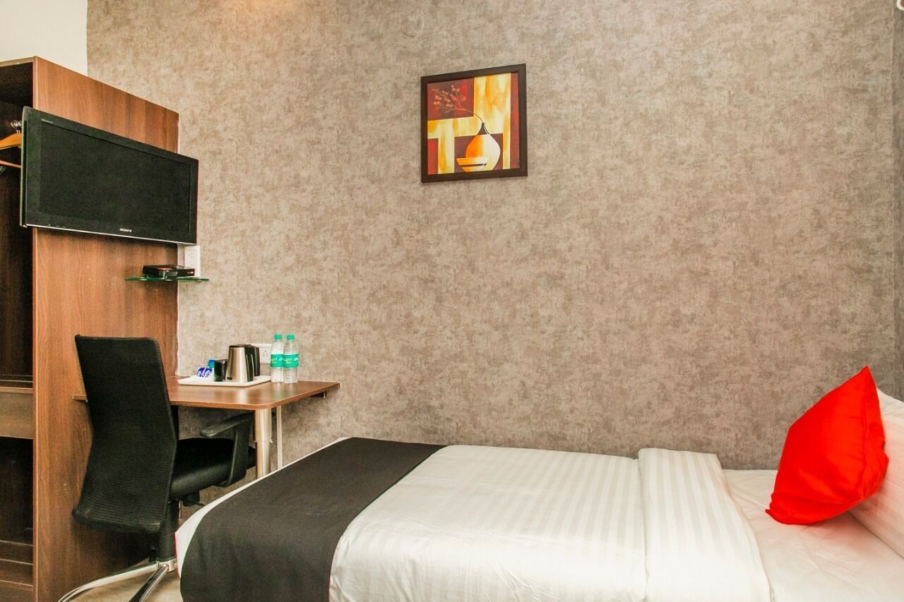 Habitación de hotel con una cama, un escritorio con silla, un televisor y un cuadro en la pared.
