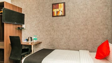 Habitación de hotel con una cama, un escritorio con silla, un televisor y un cuadro en la pared.