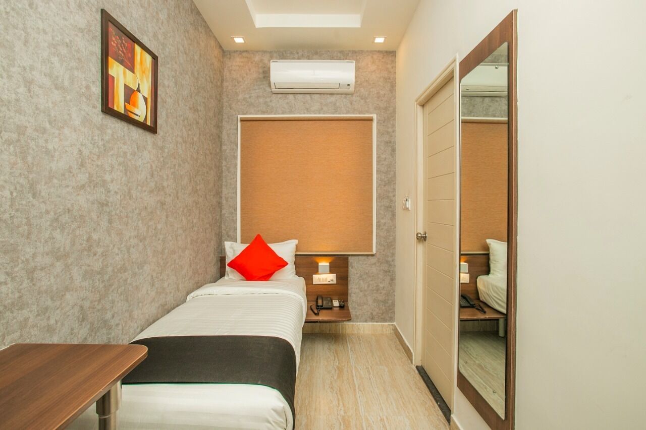 A compact hotel room with a bed, bedside table, and an air conditioning unit.
