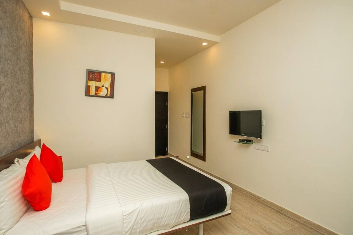 A hotel room with a bed, a TV, a mirror, and a painting on the wall.