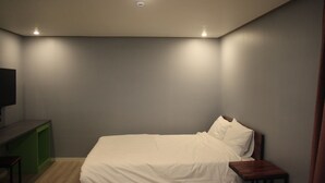 Une chambre à coucher avec un lit, une petite table de chevet en bois, un bureau vert et un téléviseur posé sur un meuble.