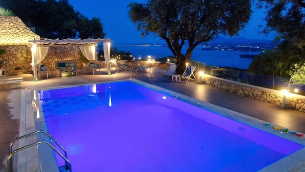 Un área de piscina con muro de piedra, sillones reclinables y una pérgola con luces.