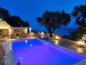 A pool area with a stone wall, lounge chairs, and a pergola with lights. - Villa Athiri Corfu with Private Pool  (Corfu)