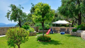Un patio trasero con césped, un árbol, un pequeño jardín, una zona de barbacoa y un tobogán.