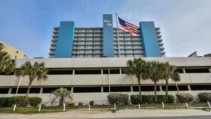 Een hotel met meerdere verdiepingen, een blauwe gevel, een Amerikaanse vlag en palmbomen op de voorgrond.