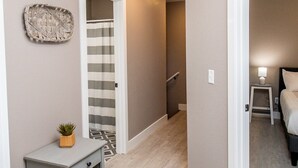 A hallway with a grey nightstand, a potted plant, and a striped shower curtain. - Frene Valley Guest House (Hermann)