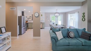 A modern living room with a teal sofa, a dining area, and a kitchen in the background. - Frene Valley Guest House (Hermann)