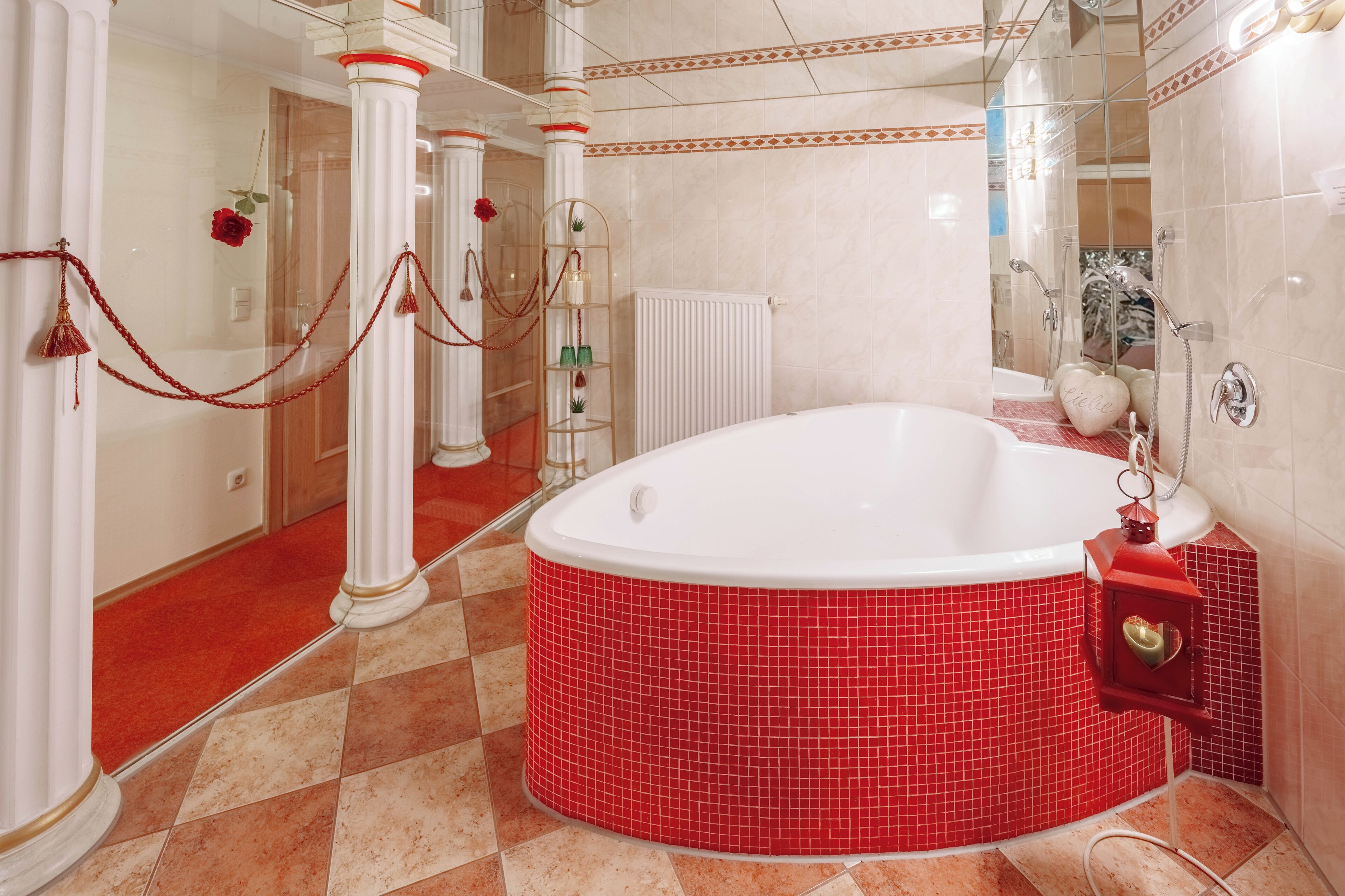 Un baño con una bañera de hidromasaje con azulejos rojos, columnas blancas y una barrera con cuerda roja.