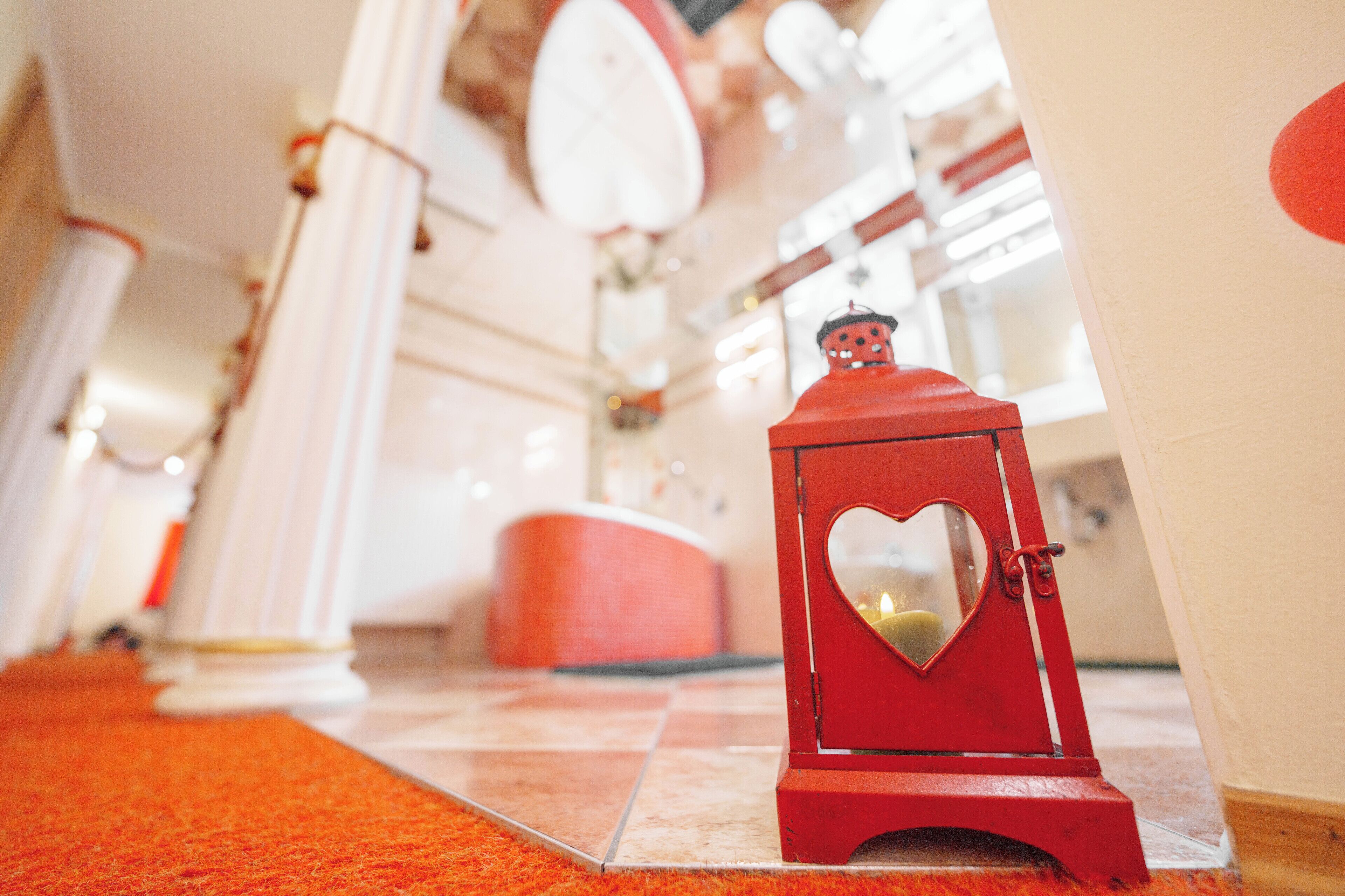A red lantern with a heart-shaped window and a figure on top, placed on a tiled floor with a red carpet in a bright, well-lit interior space.