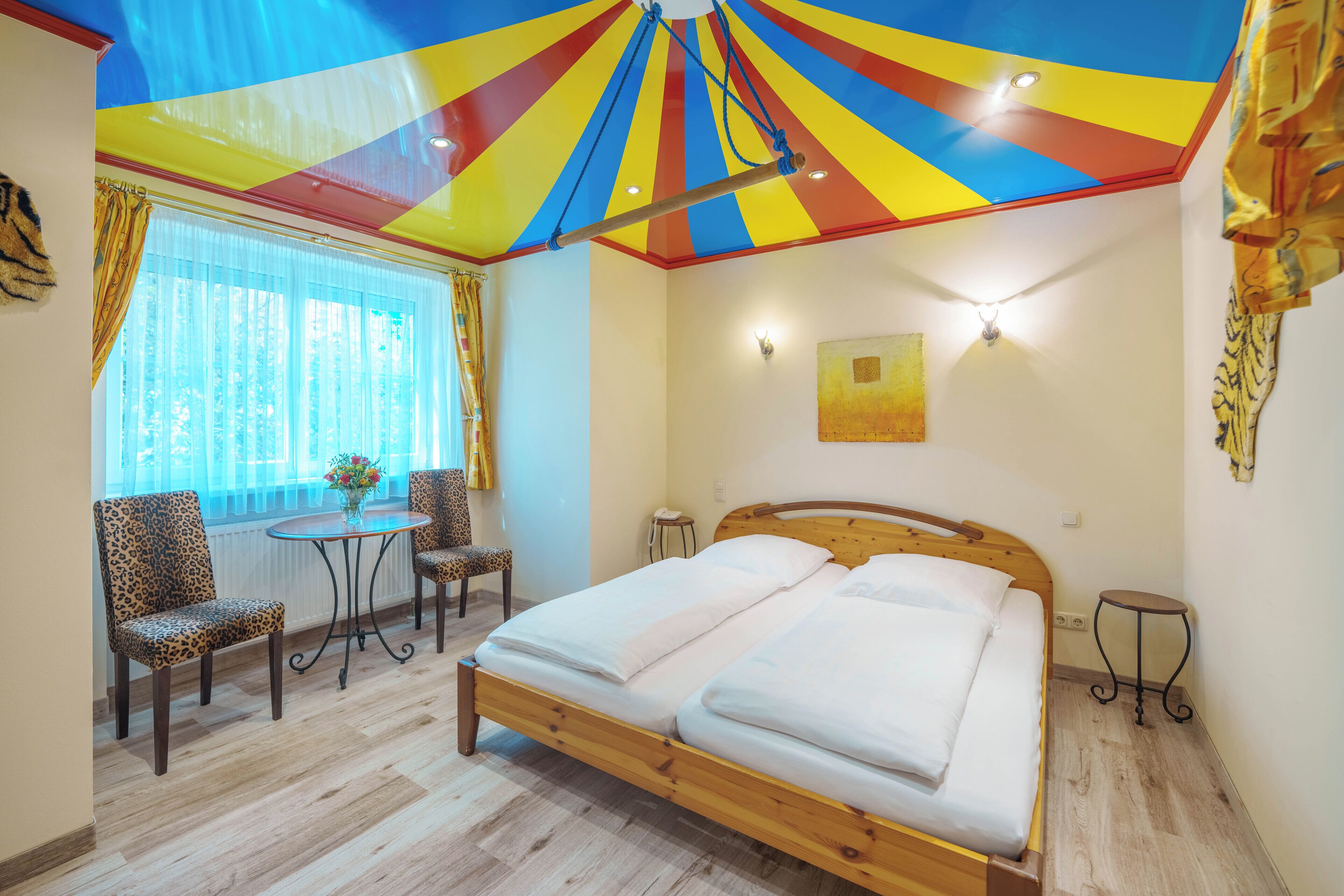 Una habitación con cama, dos sillas, una mesita y un ventilador de techo.