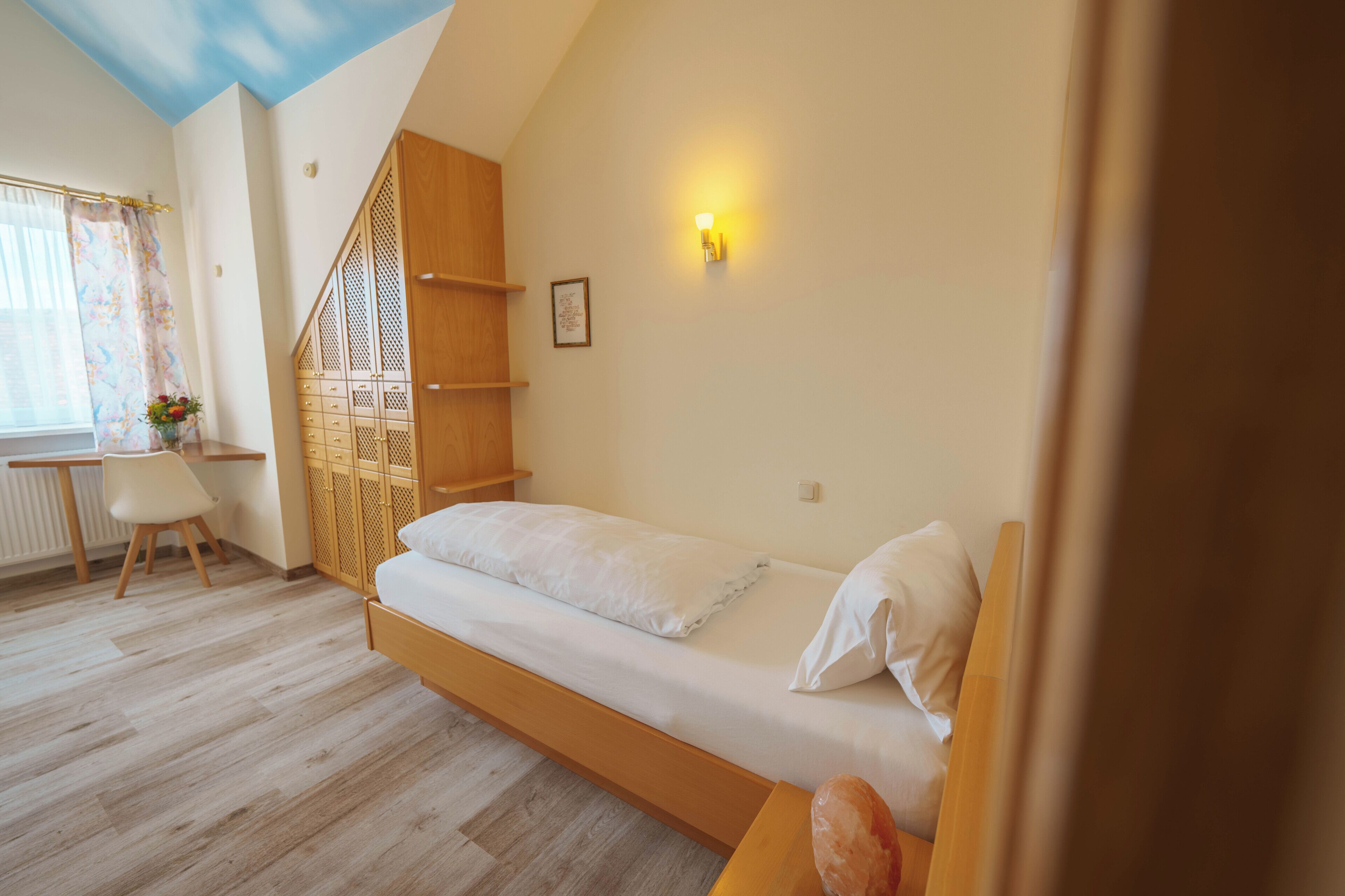 A bedroom with a wooden bed, a desk, a chair, and a window with curtains.