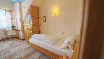 A bedroom with a wooden bed, a desk, a chair, and a window with curtains.