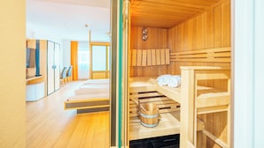 A sauna room with wooden benches, a towel rack, and a wooden bucket. - König Ludwig Designhotel (Altötting)