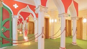 A corridor with white columns, green door, and red walls. - König Ludwig Designhotel (Altötting)