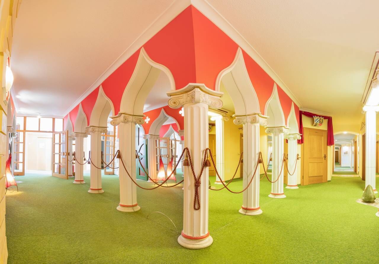 Un vestíbulo de hotel con alfombra verde, columnas blancas y paredes a rayas rojas y blancas.