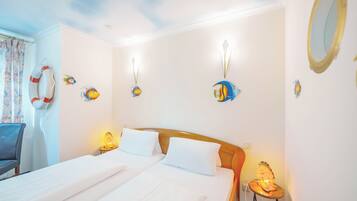A hotel room with two beds, a wooden headboard, a small table with a lamp, and wall decorations including fish and a lifebuoy.