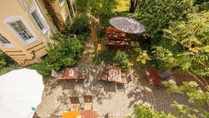 An outdoor patio with stone flooring, wooden furniture, and a large umbrella. - König Ludwig Designhotel (Altötting)
