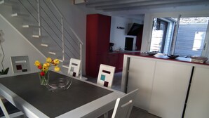 A modern kitchen with white cabinets, a red accent wall, and a dining area with a table and chairs. - VILLA with garage and terrace 200 ml beaches parks and shops (Saint-Malo)