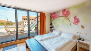 Ein Hotelzimmer mit großem Fenster, einem Bett, einer Bank und einem Orchideen-Wandbild.