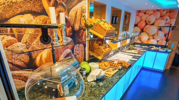 Ein reichhaltiges Buffet mit verschiedenen Speisen und einer großen Wandmalerei von Backwaren im Hintergrund.